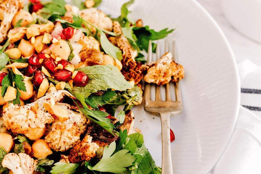 Roasted cauliflower salad with chickpeas, pomegranate seeds, herbs, and cashews on a white plate.