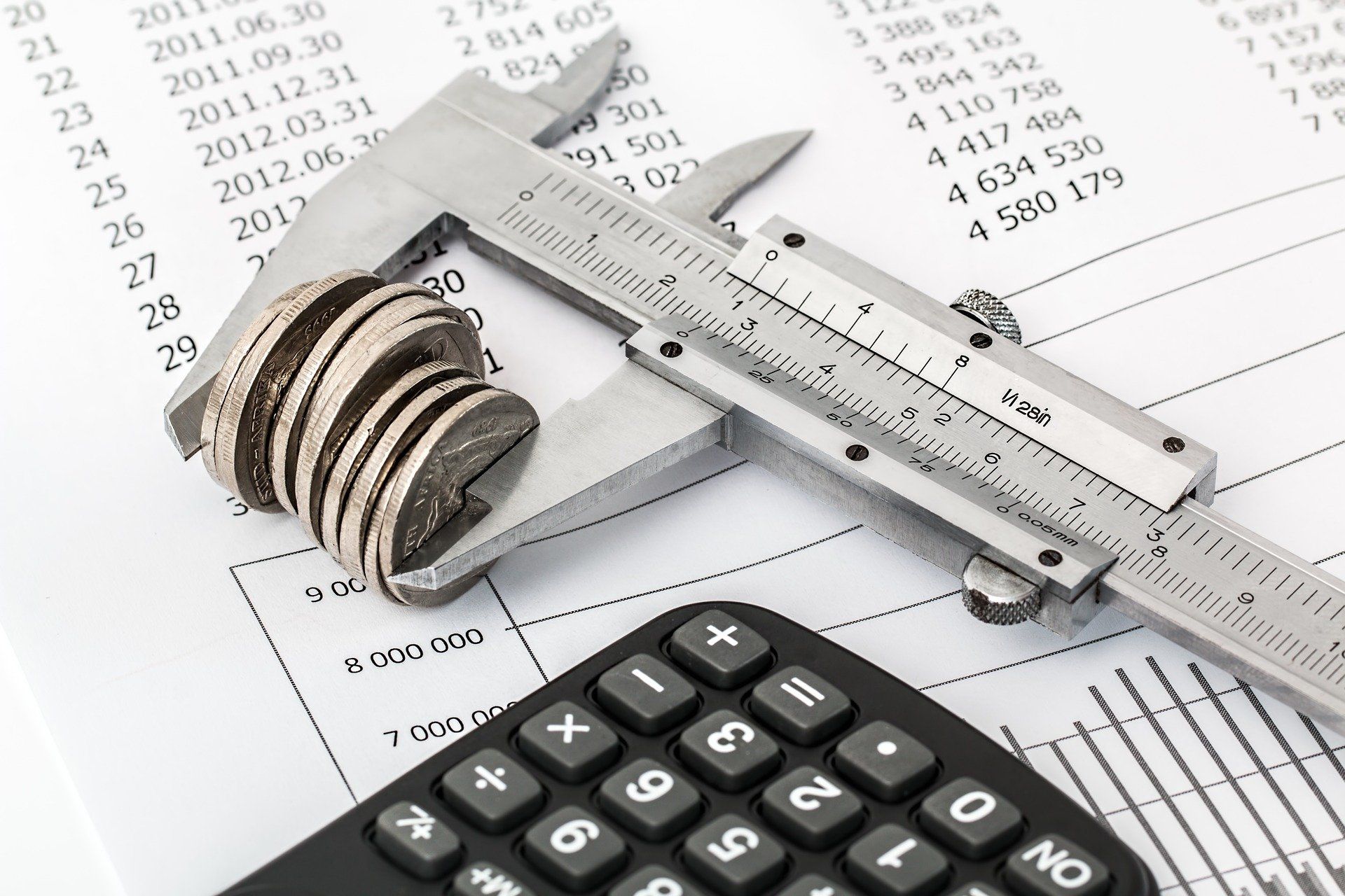 Vernier caliper measuring a stack of coins on top of financial documents, with a calculator in the foreground.
