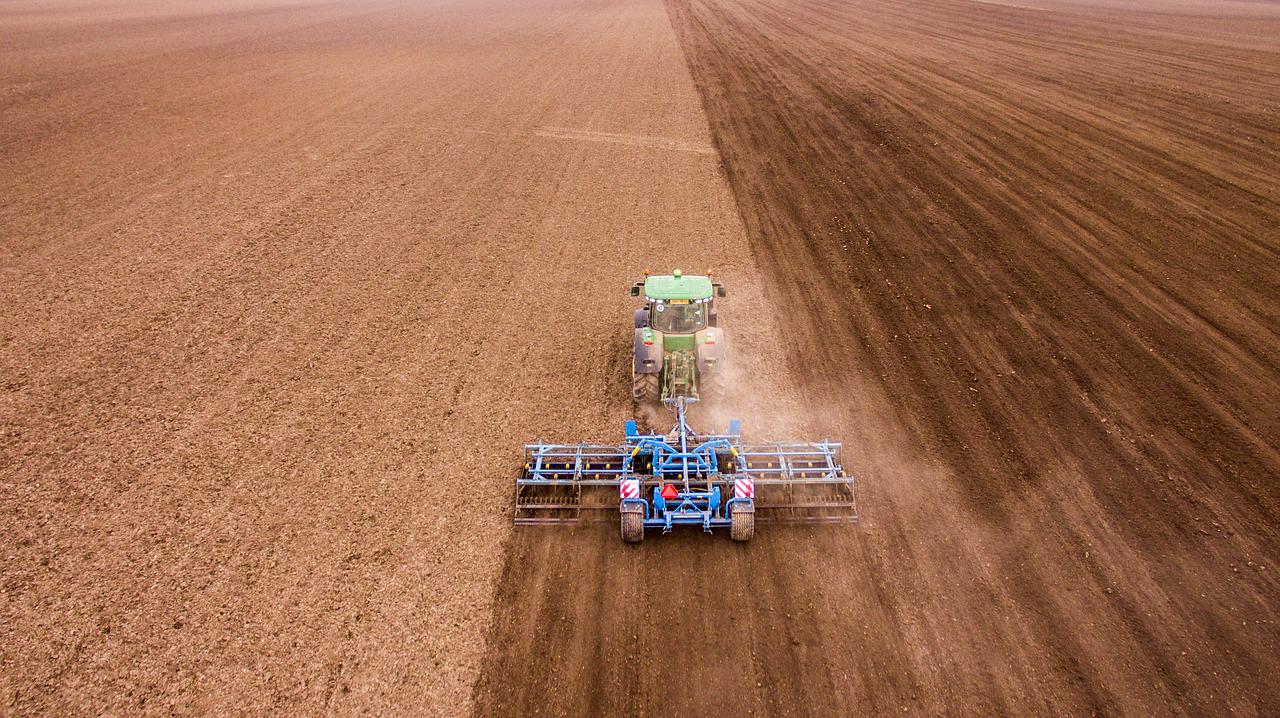 Tractor plowing a field, creating a contrast in soil color between the plowed and unplowed sections.