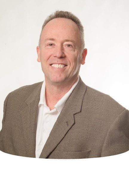 Smiling man in a blazer and white shirt. Neutral background.