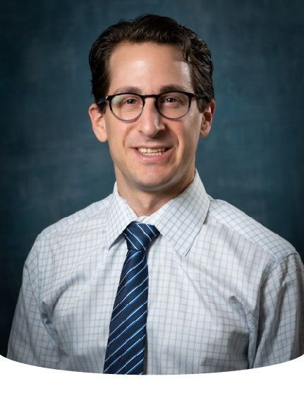 Man with glasses and a tie, smiling; on a blue background.