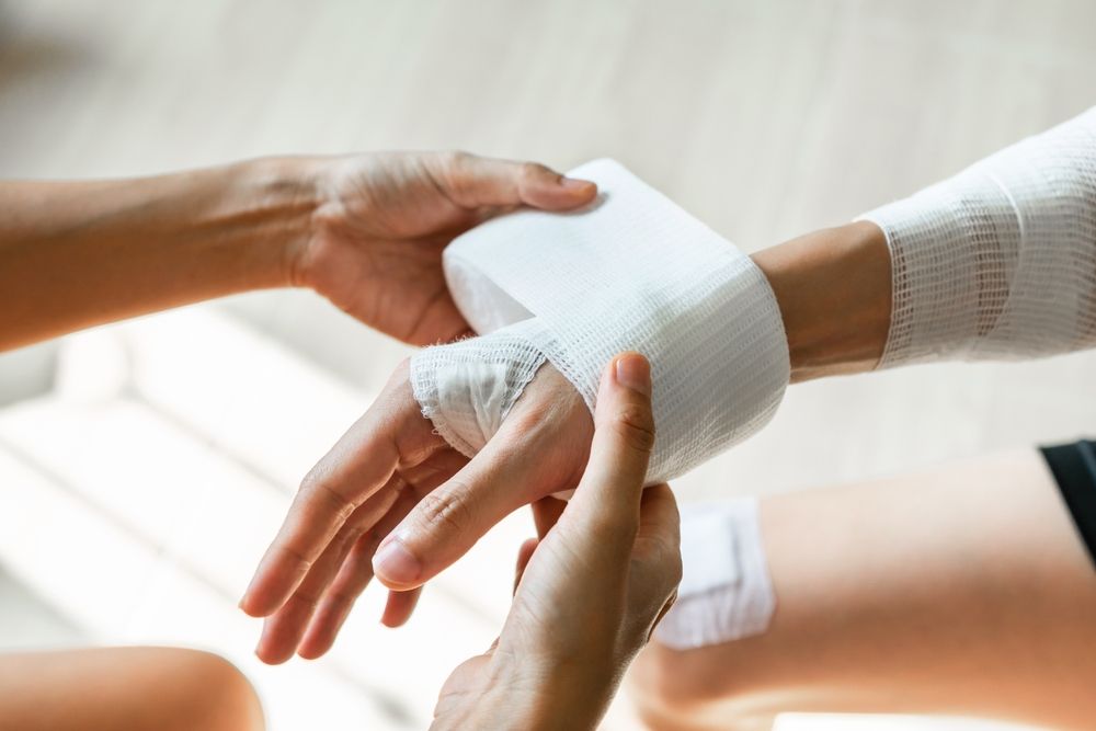 Hands wrapping a white bandage around a wrist during first aid assistance