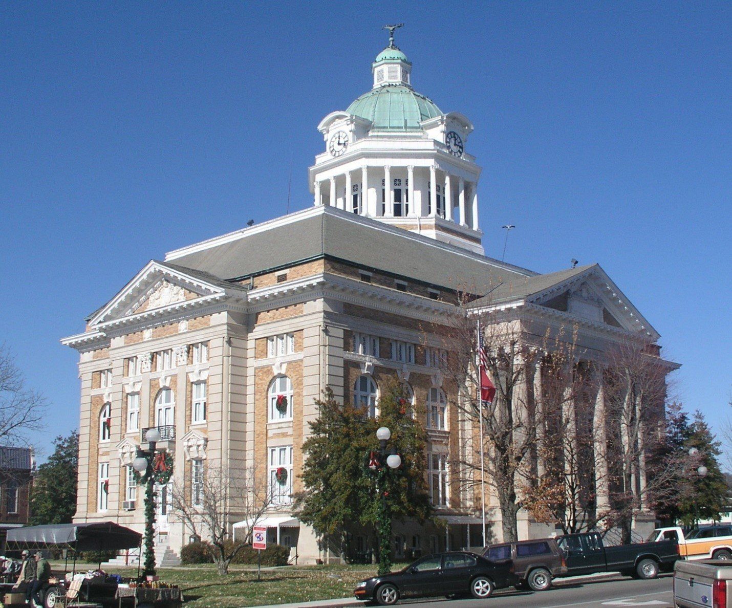 Historic courthouse with dome and columns, cars parked in front, sunny day.