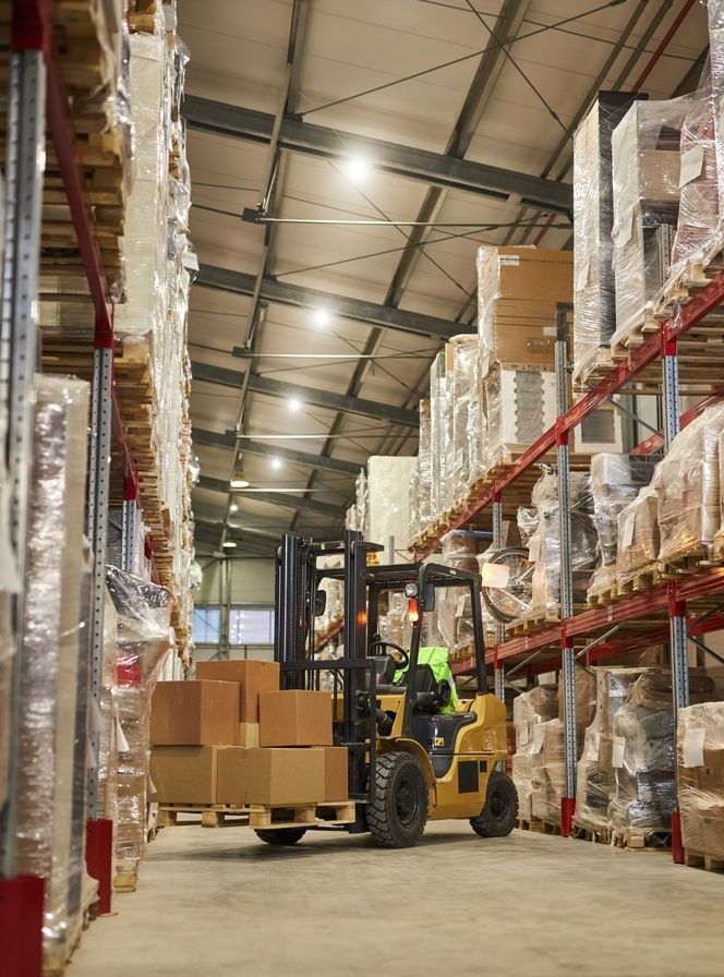 Yellow forklift carrying boxes in a warehouse with tall shelving and packages.