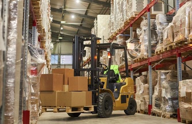 Yellow forklift carrying boxes in a warehouse.
