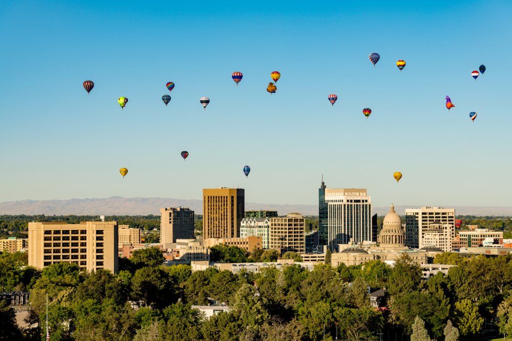Hot air balloons over Boise, Idaho skyline; blue sky, colorful balloons, buildings and trees.