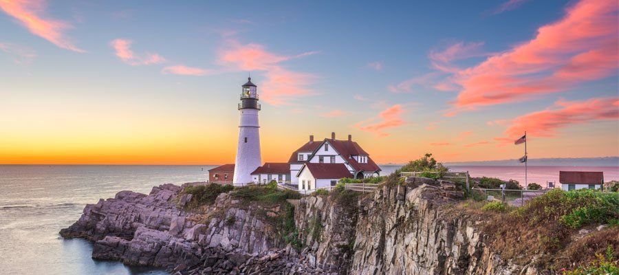 Lighthouse on a rocky cliff overlooking the ocean during a colorful sunset.
