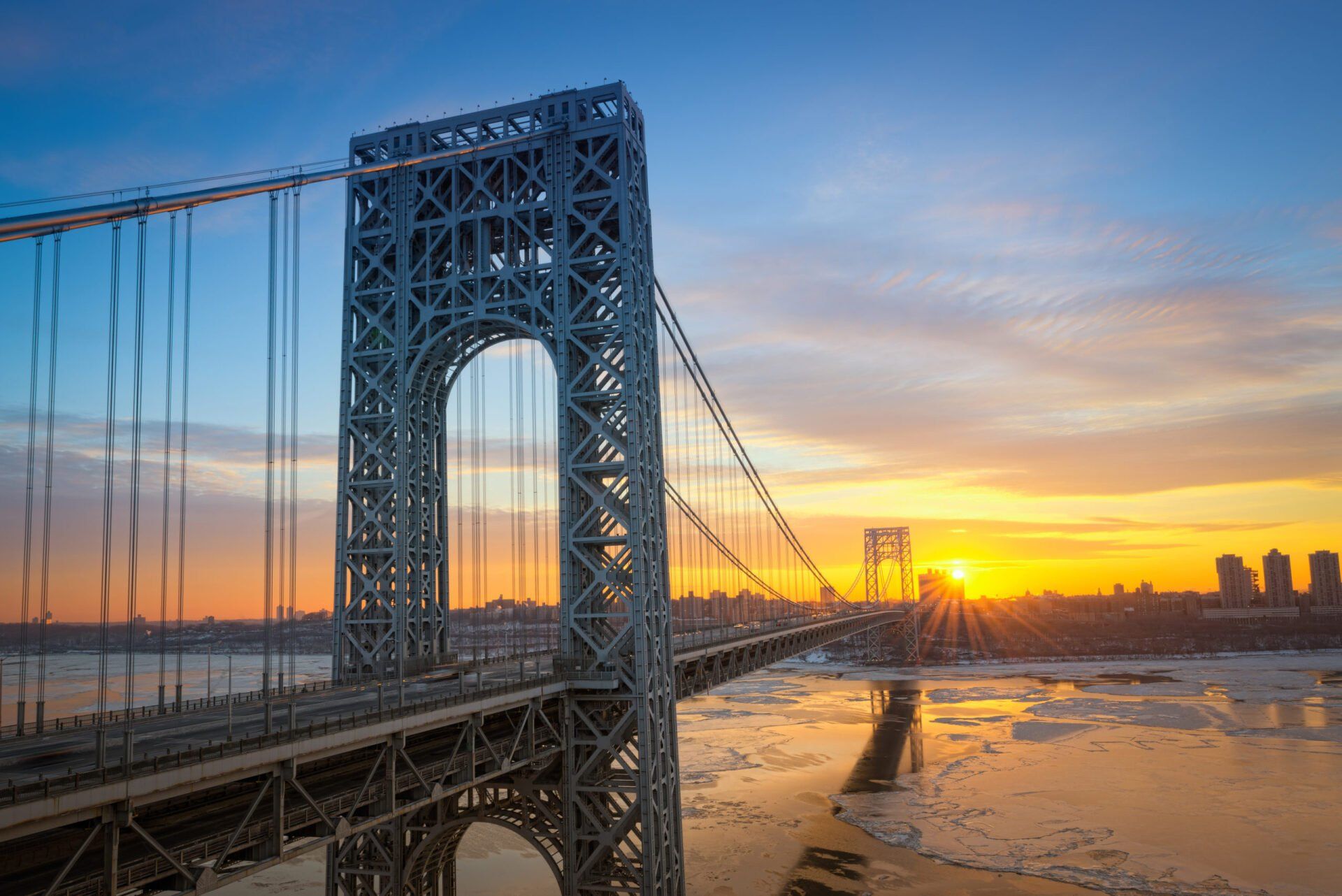 George Washington Bridge at sunrise, golden sky, icy river.