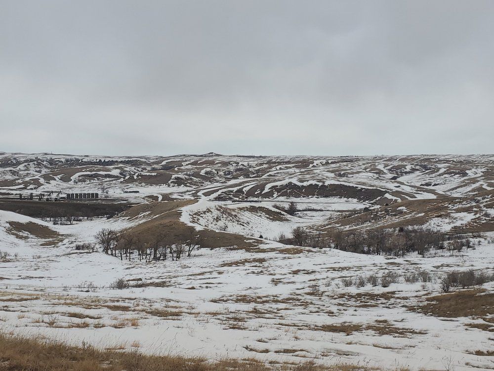 Snowy, rolling hills under an overcast sky. A sparse layer of snow covers the landscape.