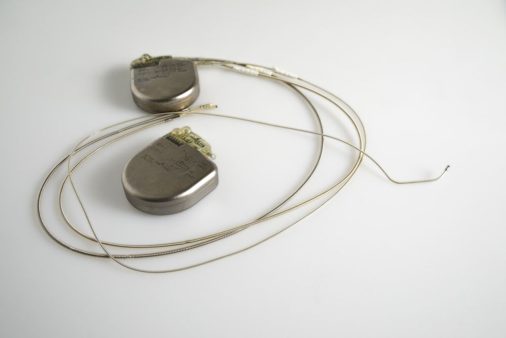 Two silver pacemakers with wires on a white surface.