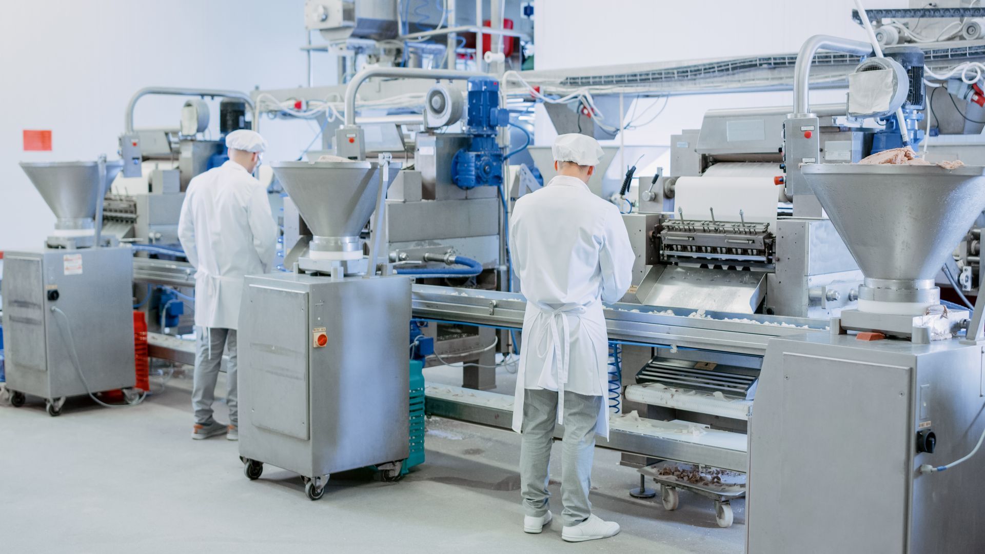 Workers in white coats operating food processing machinery in a factory.