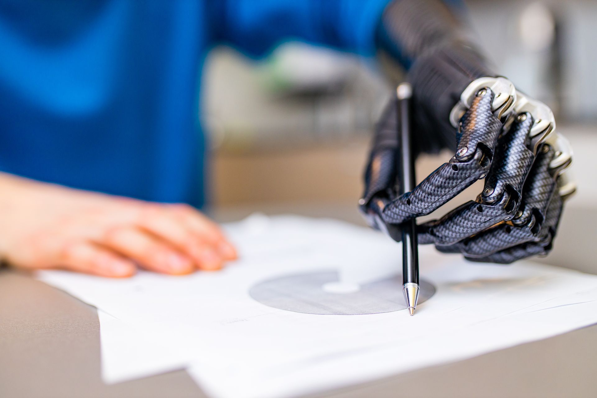 Person with a prosthetic hand holding a pen, writing on paper with a circular cutout.