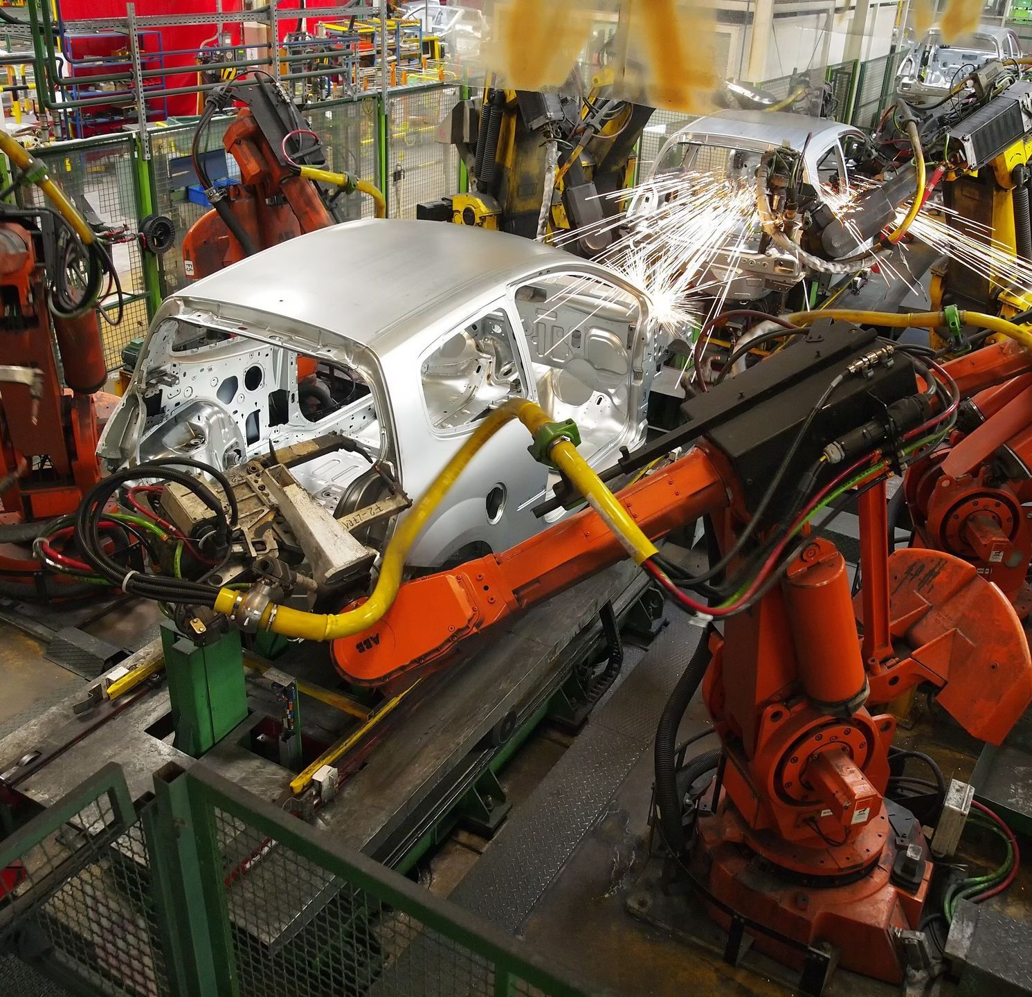 Robots welding car bodies in a factory, with sparks flying.