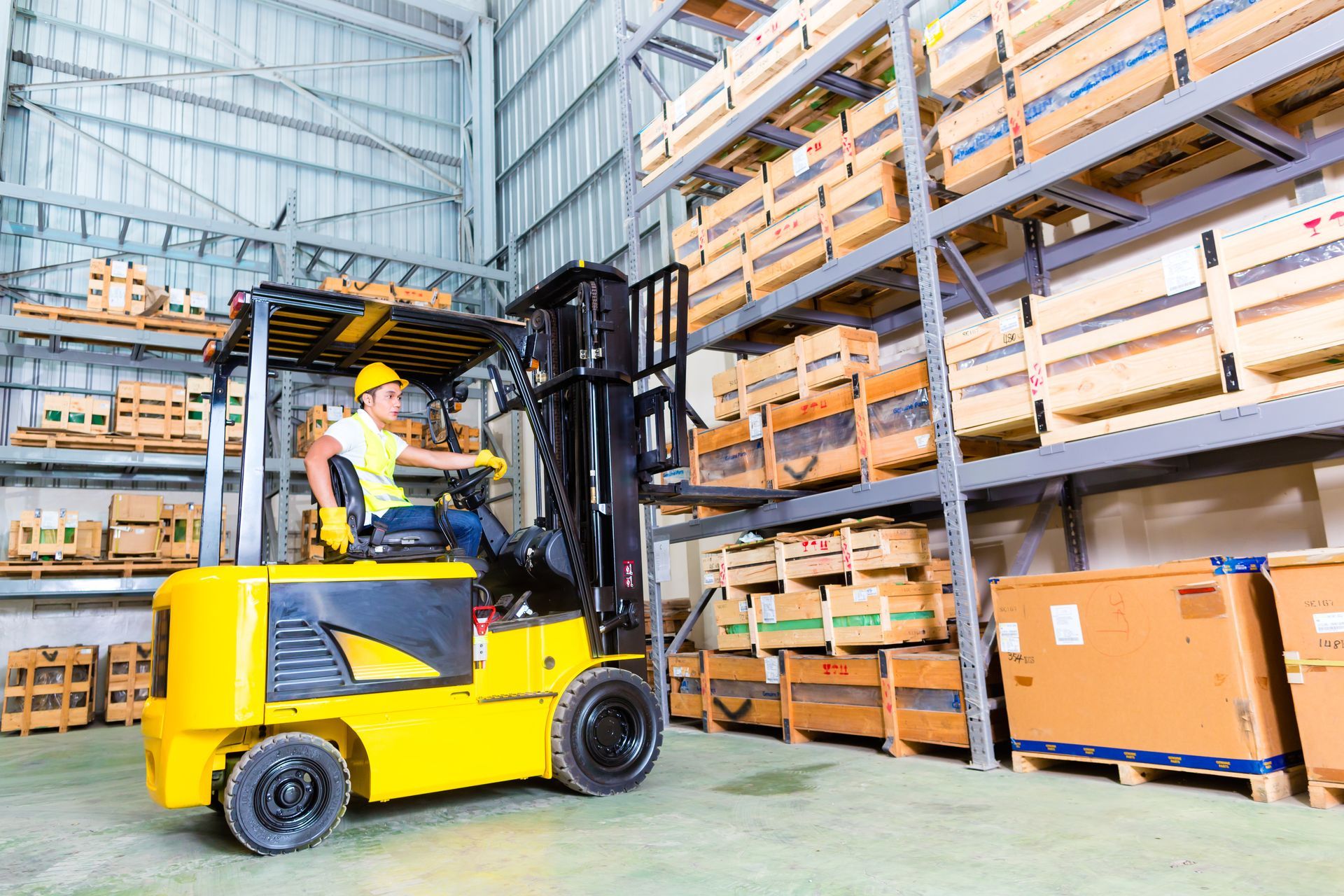 A person driving a yellow forklift in a warehouse; shelves stacked with wooden crates.