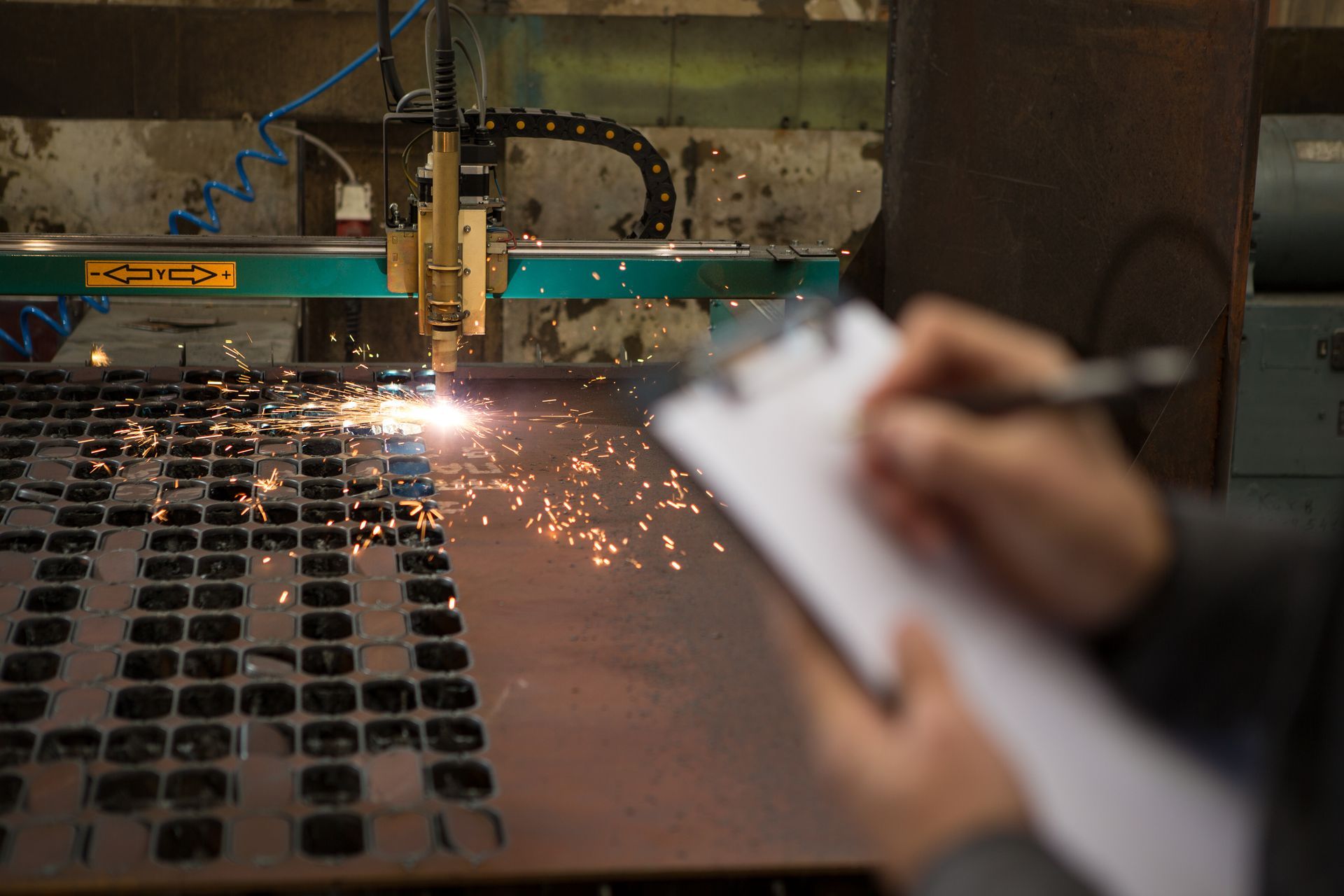 Person taking notes while industrial laser cuts metal with sparks.