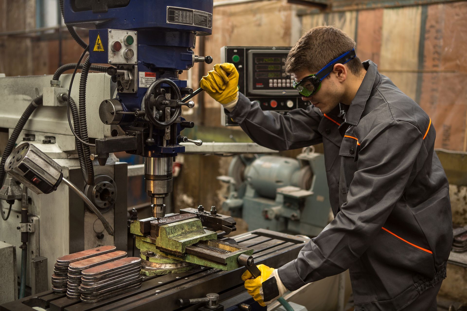 Man operating a milling machine in a workshop, wearing safety glasses and gloves.