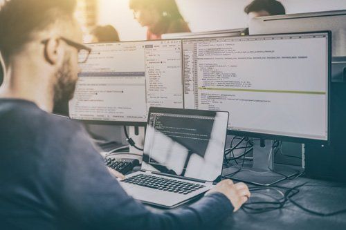 Man coding on laptop and dual monitors in office setting.