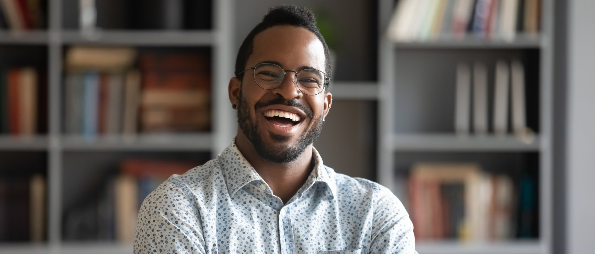 Smiling Black man with glasses stands in front of a bookshelf.