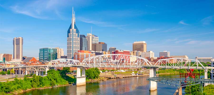 Nashville, Tennessee skyline with a white bridge and buildings along a river under a clear blue sky.