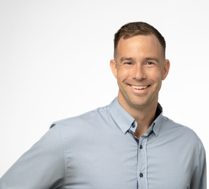 Man smiling, wearing a light blue button-down shirt, white background.