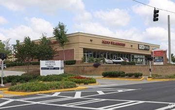 Retail storefront in a shopping center with parking lot, landscaping, and a traffic light overhead