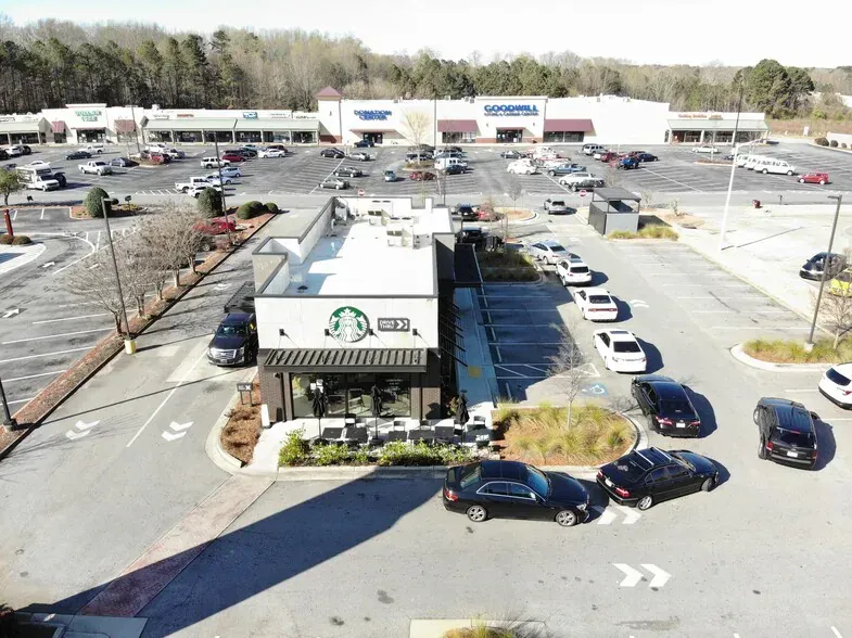 Aerial view of a Starbucks drive-thru and parking lot with cars in a shopping center.