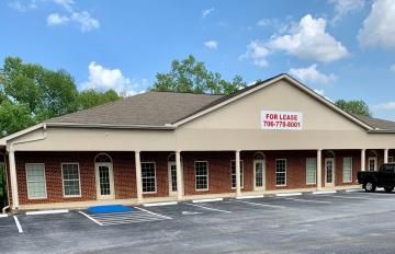 Single-story brick office building with a “For Lease” sign and parking lot