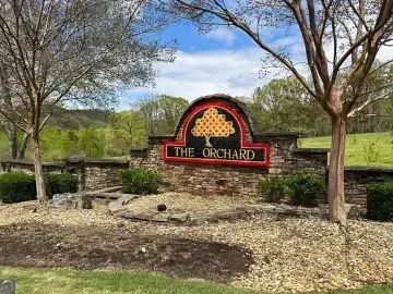 “The Orchard” entrance sign in a landscaped park with trees and rocks