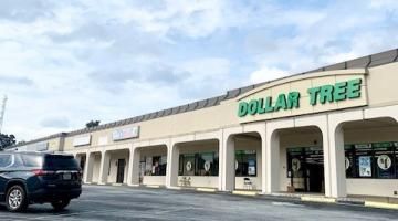 Dollar Tree storefront in a strip mall with a black SUV parked outside under a cloudy sky