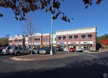 Shopping center storefronts with parked cars on a sunny day