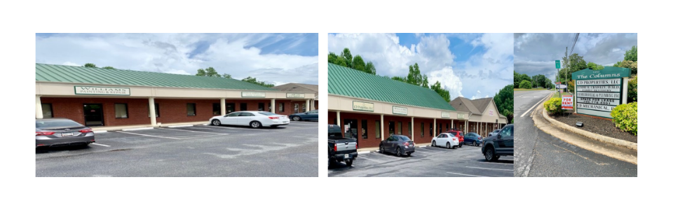 Strip mall storefront with parked cars and a sidewalk ramp beside flower beds