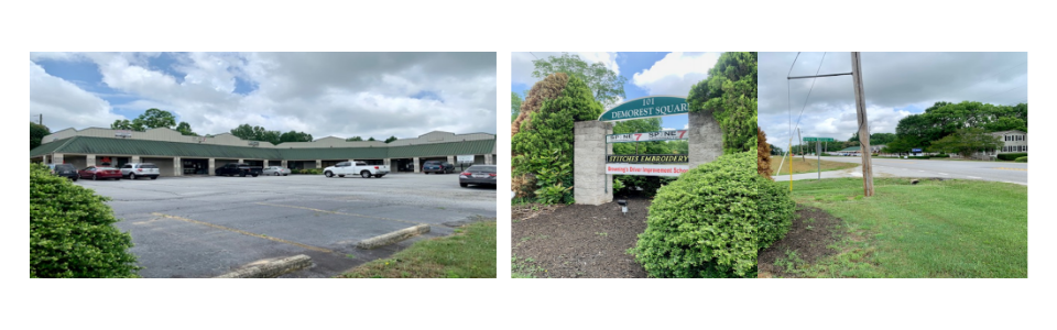 Strip mall parking lot with storefronts and a landscaped entrance sign under cloudy skies