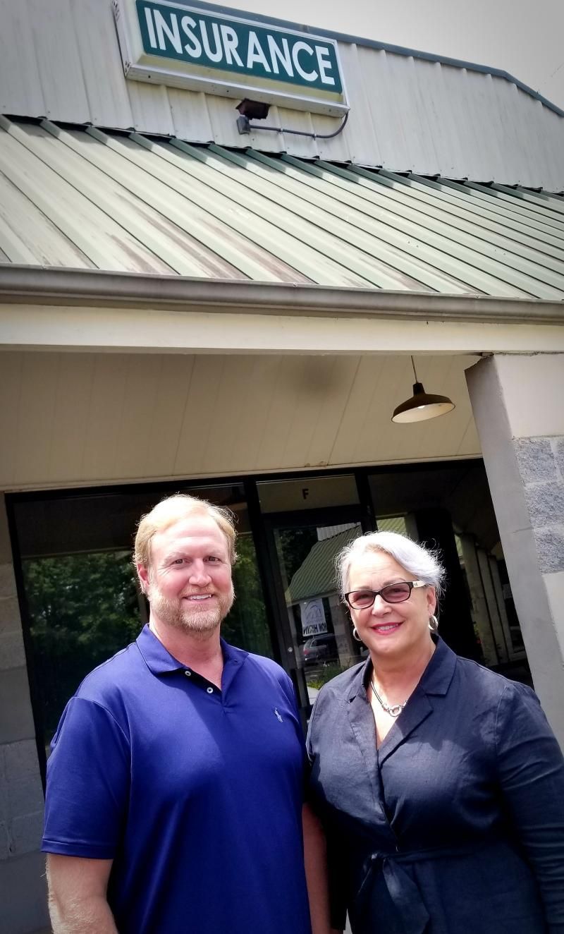 Two people standing outside an insurance office, smiling beneath a green roof sign.