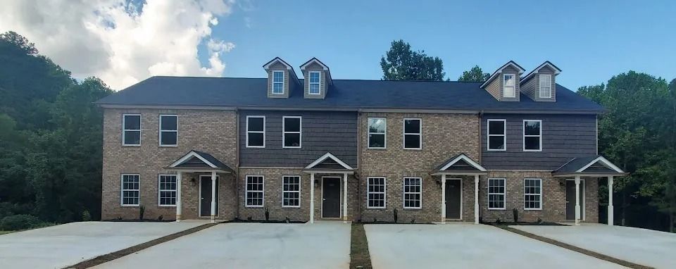 Two-story brick townhouses with dormer windows and shared driveway in a wooded setting