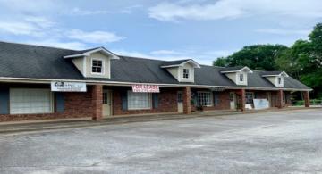 Brick strip mall storefronts with dormer windows and empty parking lot under a cloudy sky