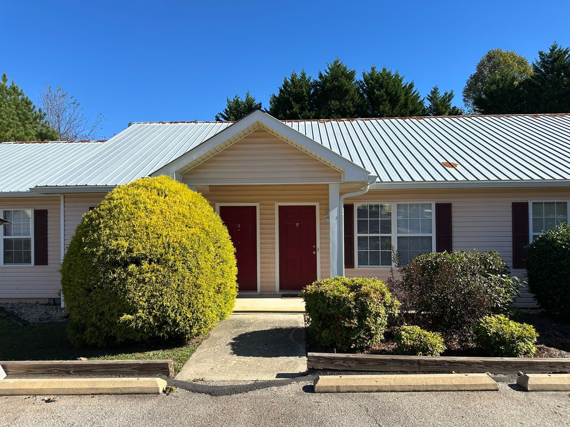 Single-story house with red doors, white roof, and trimmed bushes in front yard