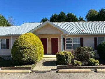 Single-story house with white roof, red front doors, and trimmed shrubs along a walkway