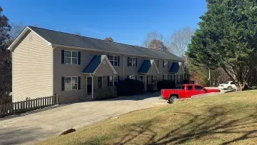 Suburban two-story beige house with dark shutters and a red pickup truck parked in the driveway.