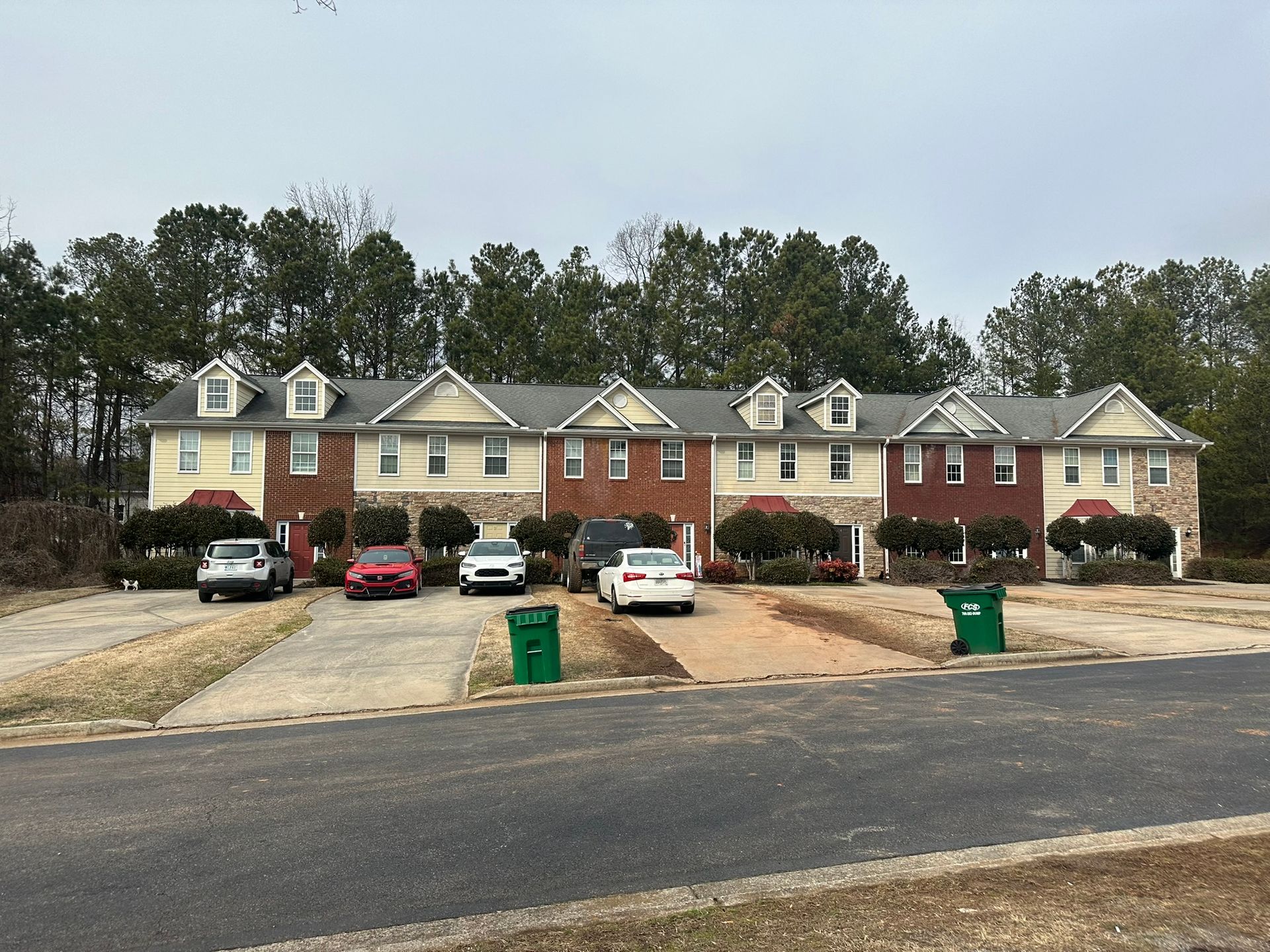 Row of townhouses with parked cars and green trash bins along a paved street