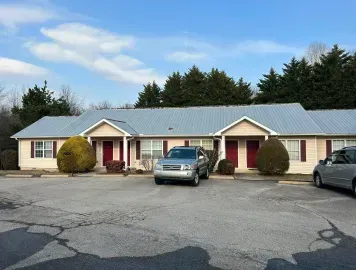 Single-story motel with red doors and parked cars in front under a cloudy sky