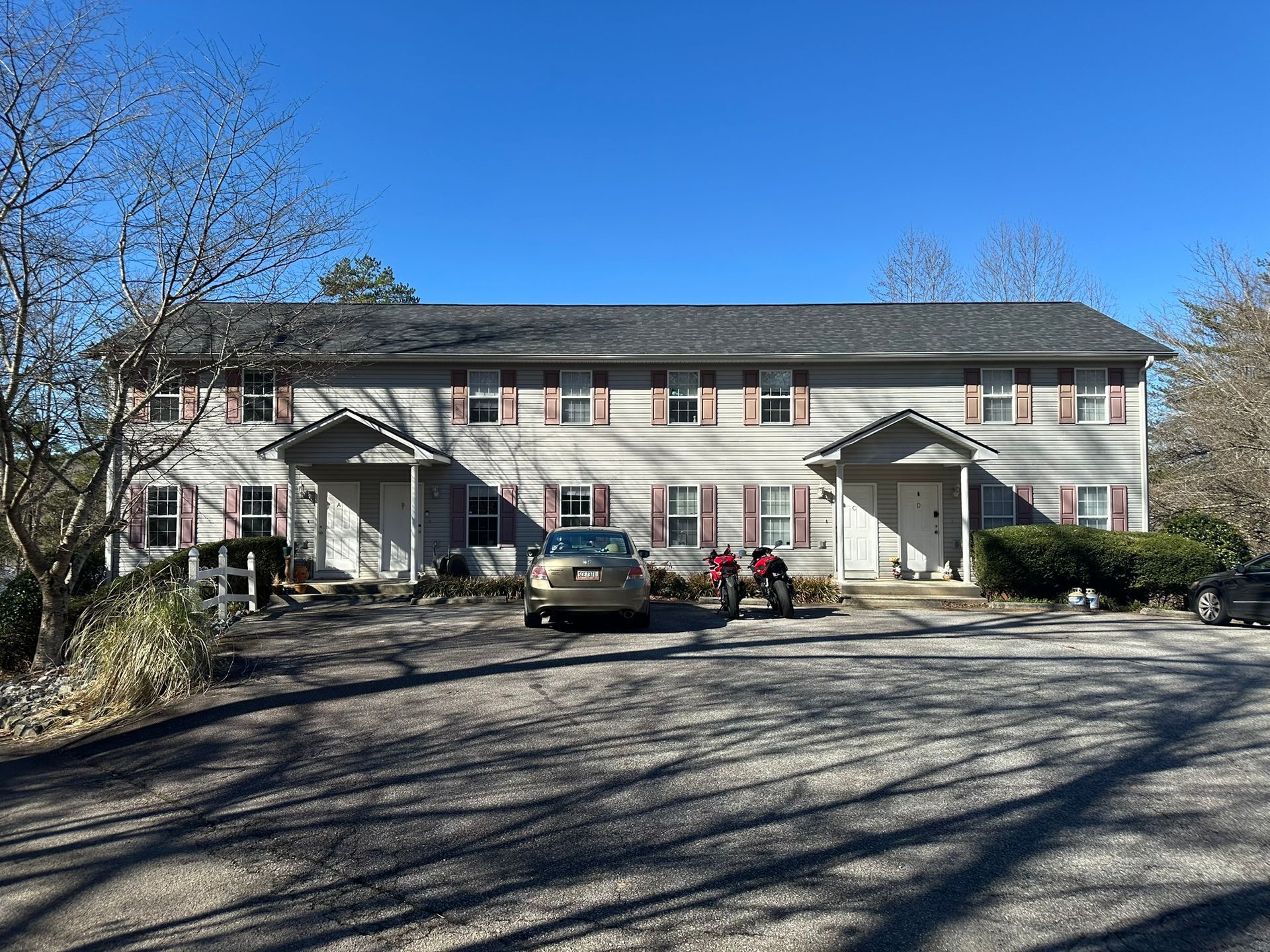 Two-story apartment building with parked cars in front and leafless trees under a clear blue sky