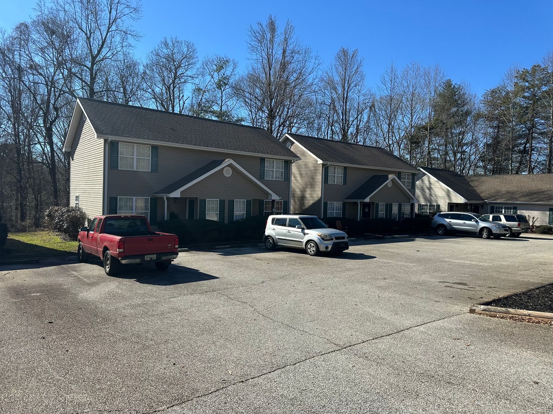 Apartment buildings with parked trucks and cars in a gravel lot under a clear blue sky