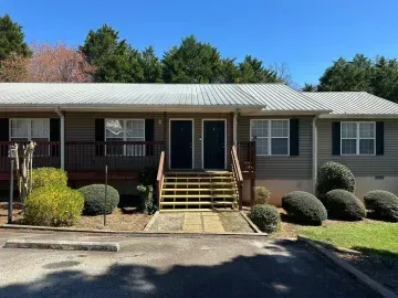 Single-story brick building with front steps, double doors, and shrubs under a clear blue sky