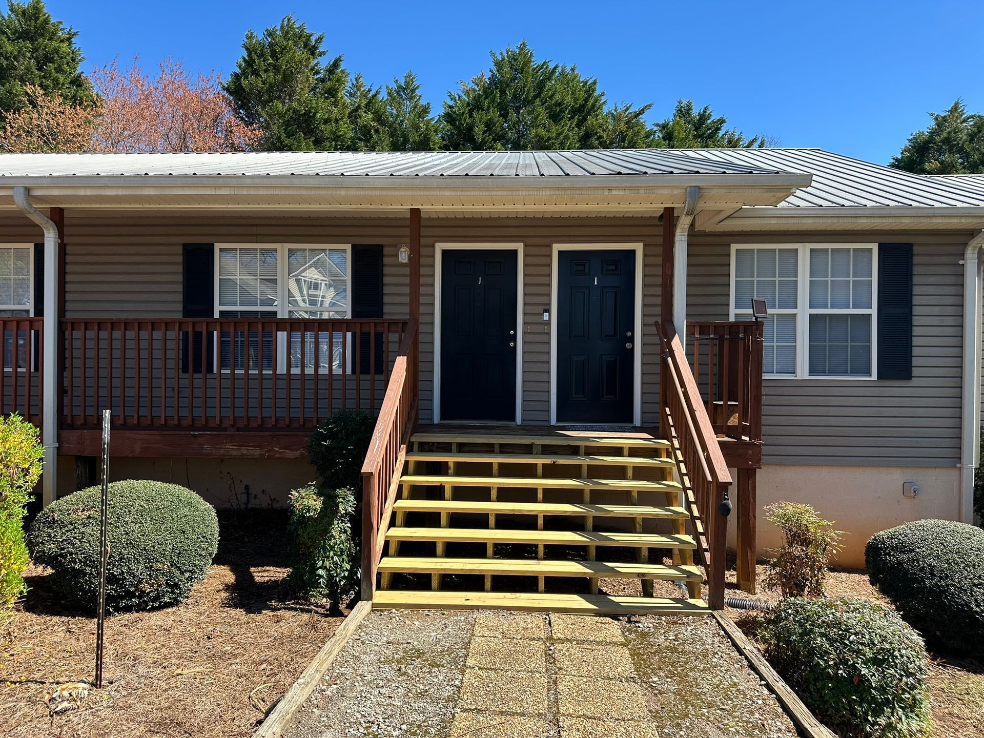 Front porch with yellow steps and dark double doors on a beige house under a clear blue sky