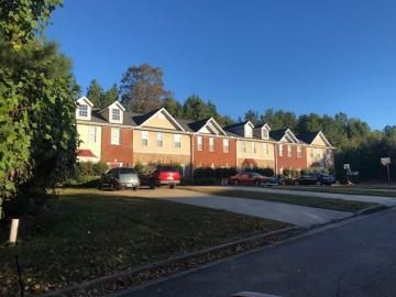 Row of red-brick townhouses with white trim along a curved driveway under a clear blue sky