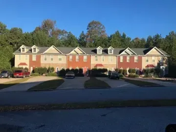 Row of tan and red townhouses with parked cars in front under a clear blue sky.