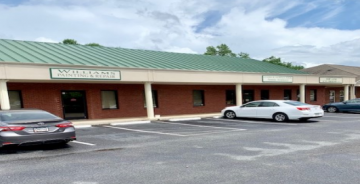 Strip mall storefront with a green roof and two parked cars in front