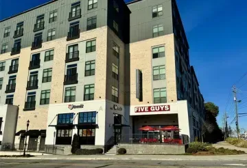 Street-level view of a building with a Five Guys restaurant and a café on the corner under a blue sky