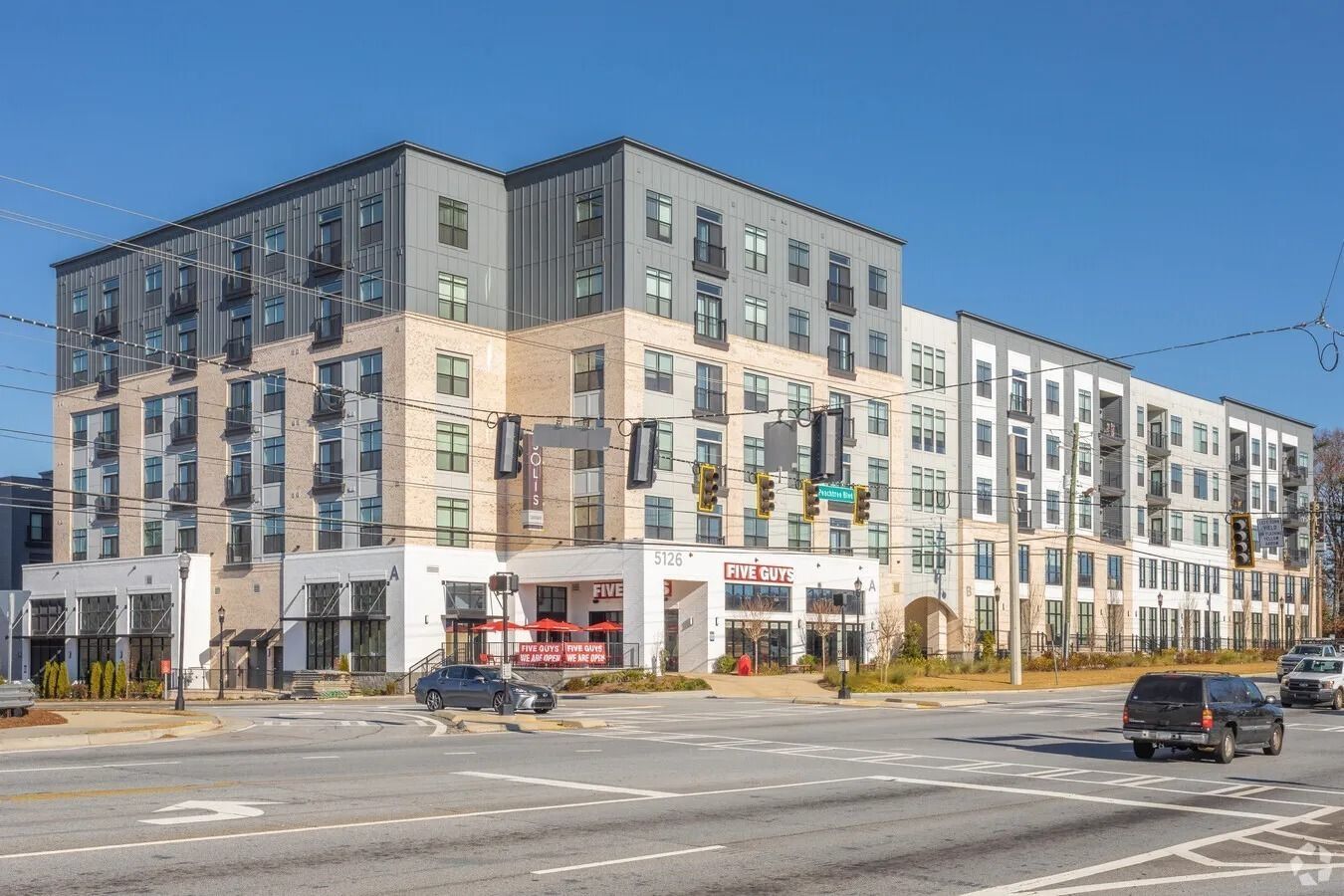Modern apartment building with retail shops along a busy city street under a blue sky