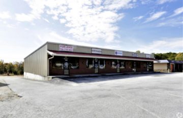 Strip mall storefronts with empty parking lot under a cloudy sky